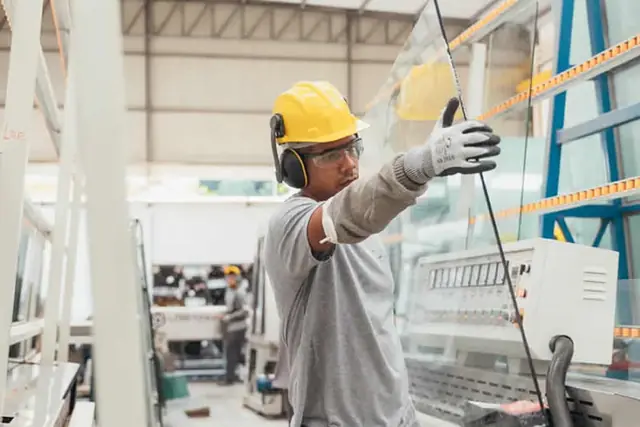 Trabalhador com protetor auricular e luvas operando máquina industrial
